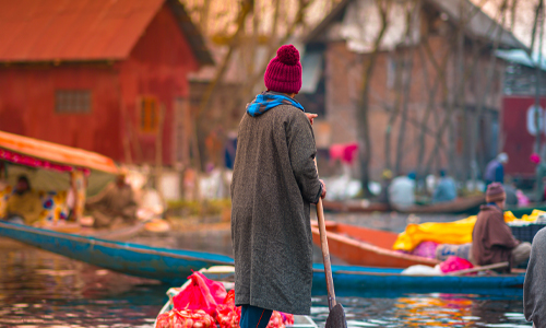 A man in a hat skillfully maneuvers a boat across the tranquil water surface.