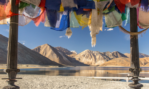 A serene landscape of mountains and a lake adorned with colorful prayer flags fluttering in the wind.